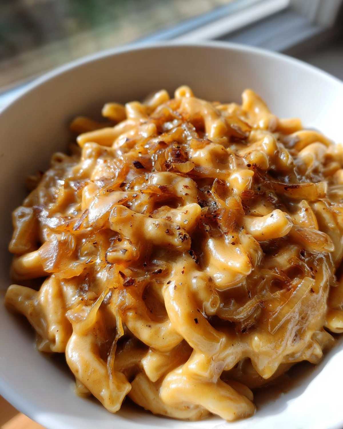 Close-up of creamy french onion pasta topped with caramelized onions in a white bowl.