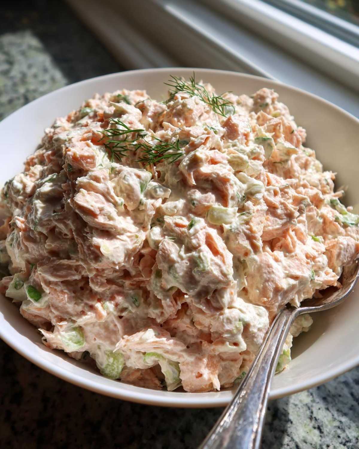 A close-up view of creamy salmon salad mixed with celery and topped with fresh dill, ready to serve.
