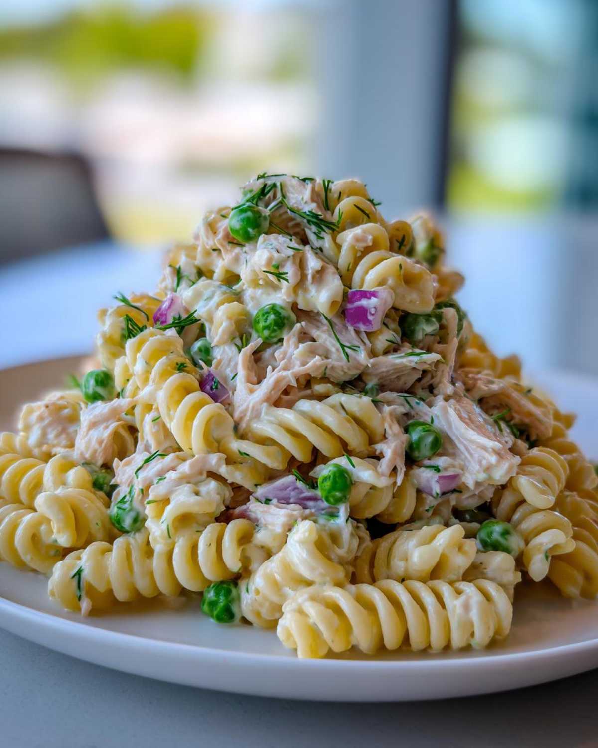 A tall mound of creamy Tuna Pasta Salad made with rotini pasta, tuna, green peas, red onion, and dill.