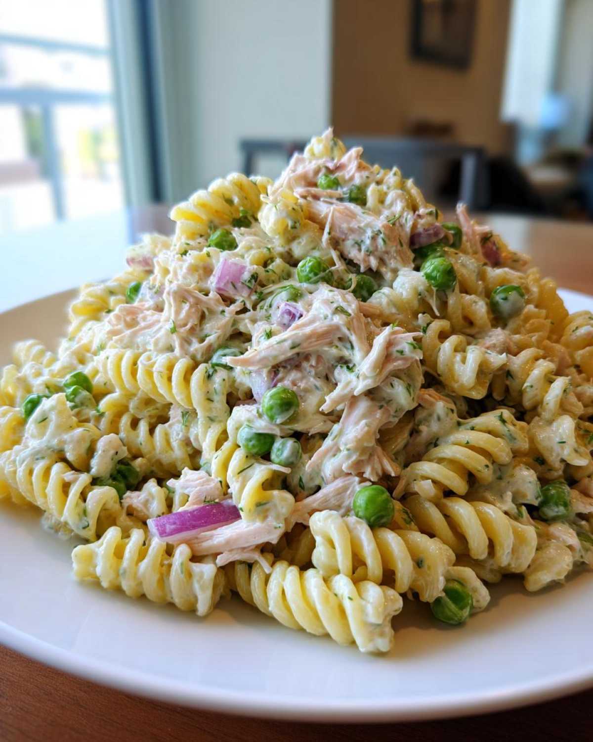 A generous serving of creamy tuna pasta salad made with rotini pasta, peas, and red onion on a white plate.
