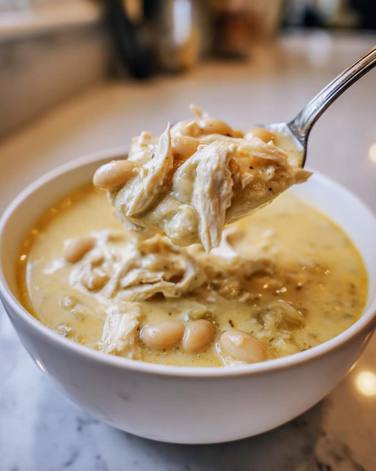 A spoonful of shredded chicken and white beans lifted from a bowl of creamy white chicken chili.