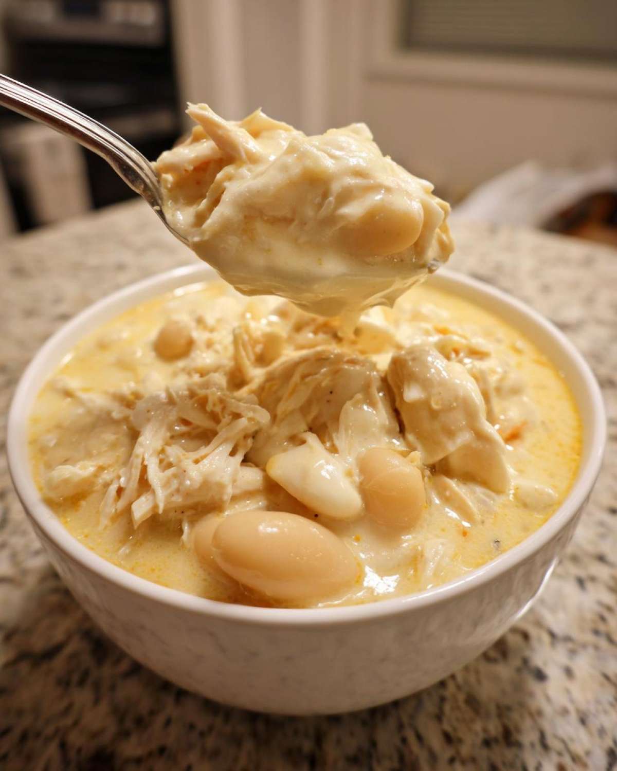 A spoonful of thick, creamy white chicken chili featuring shredded chicken and white beans being lifted from a bowl.