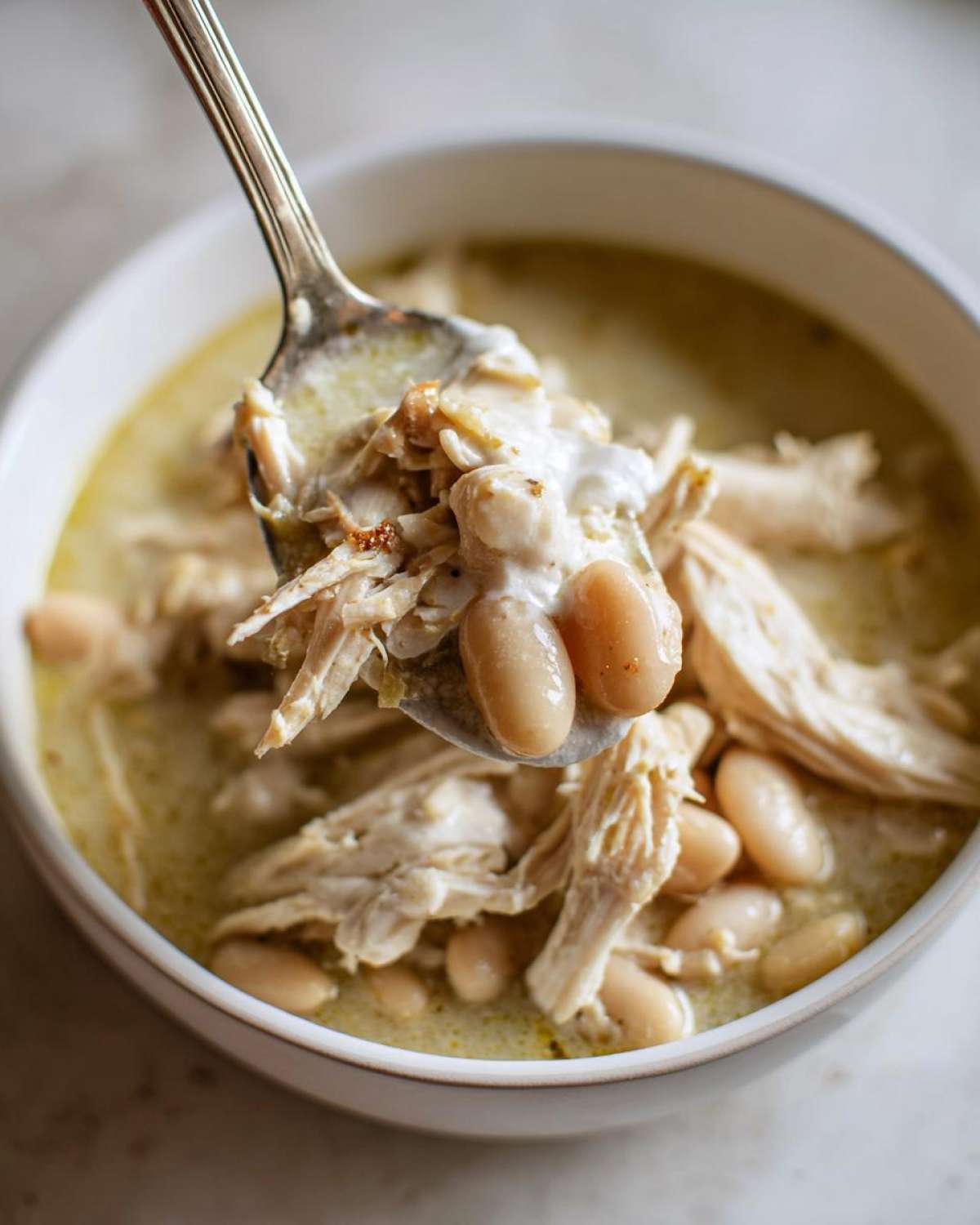 A spoonful of creamy white chicken chili, showing shredded chicken, white beans, and a dollop of cream.