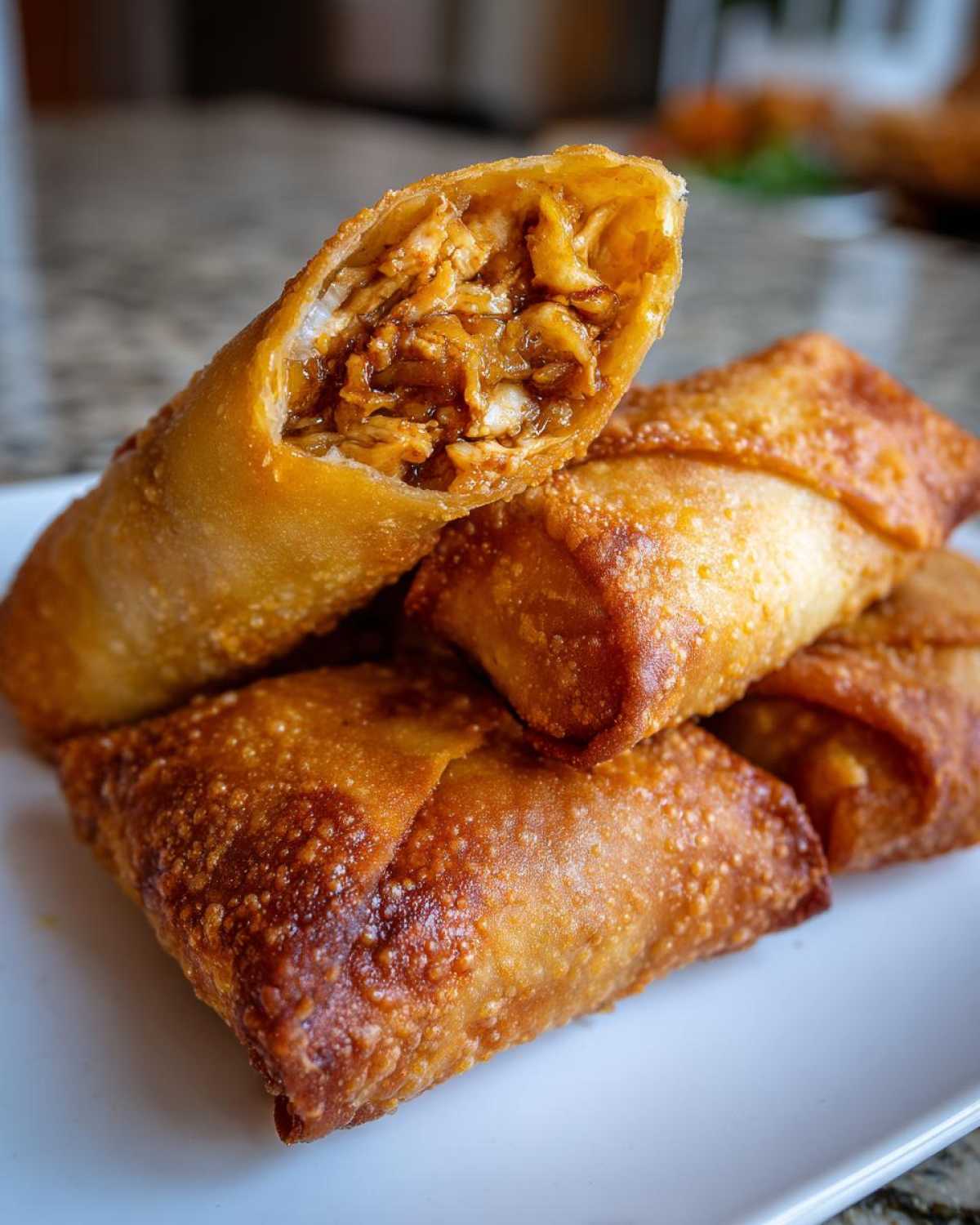 A close-up of several golden-brown, crispy fried egg roll pieces stacked on a white plate, with one cut open showing the savory filling.