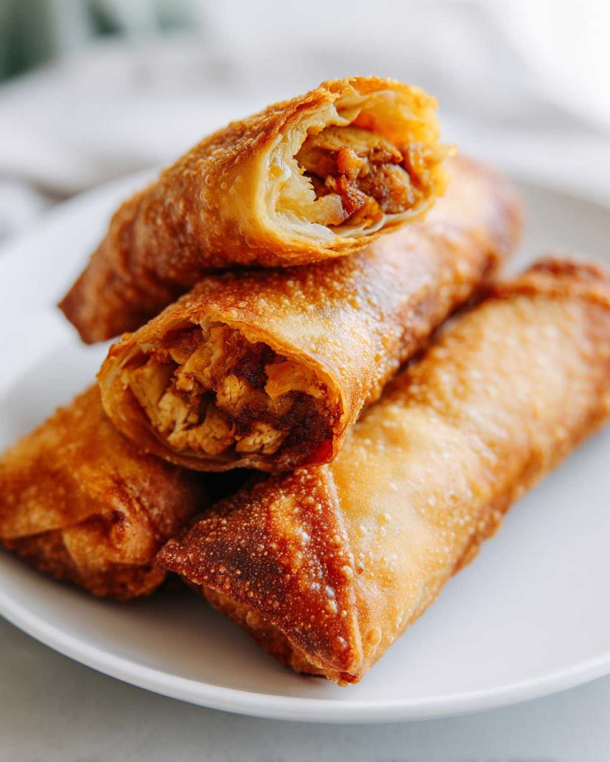 Close-up of golden brown, crispy fried egg roll, one cut open to show the savory filling.