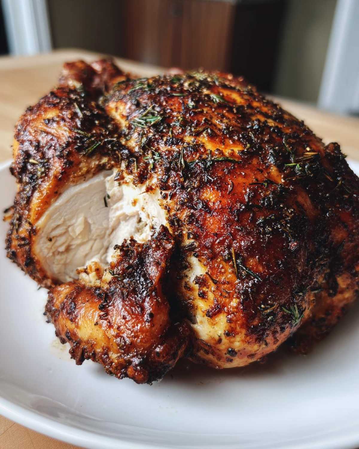 A perfectly roasted spatchcock chicken with deeply browned, crispy skin seasoned with herbs, showing a slice removed to reveal moist white meat.