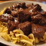 Close-up of tender crockpot beef tips smothered in rich brown gravy served over a bed of wide egg noodles.