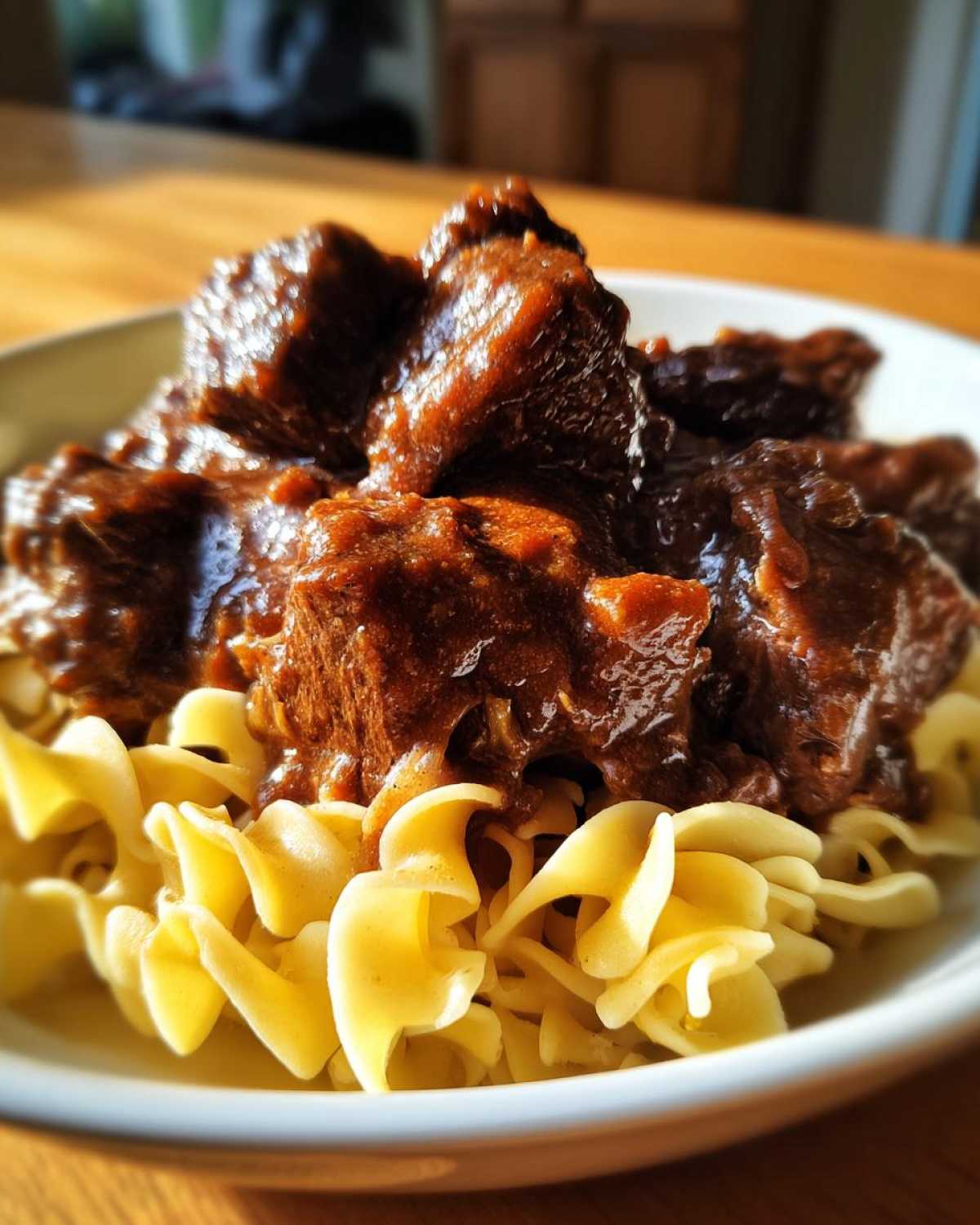 Close-up of tender crockpot beef tips smothered in rich brown gravy served over wide egg noodles.