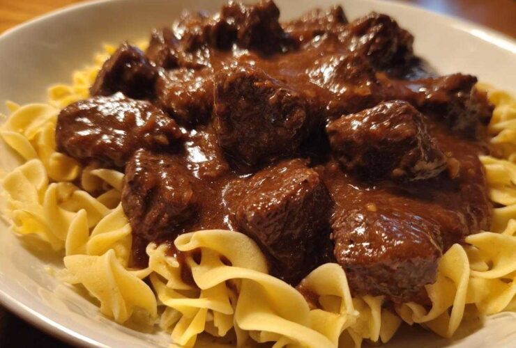 Close-up of tender crockpot beef tips smothered in rich brown gravy served over a bed of wide egg noodles.