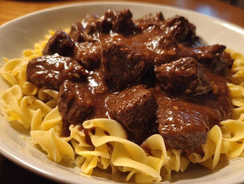 Close-up of tender crockpot beef tips smothered in rich brown gravy served over a bed of wide egg noodles.