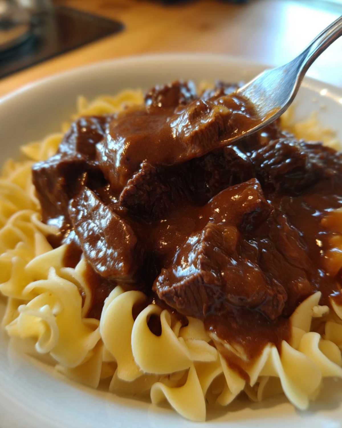 A fork lifts a piece of tender crockpot beef tips covered in rich brown gravy over egg noodles.
