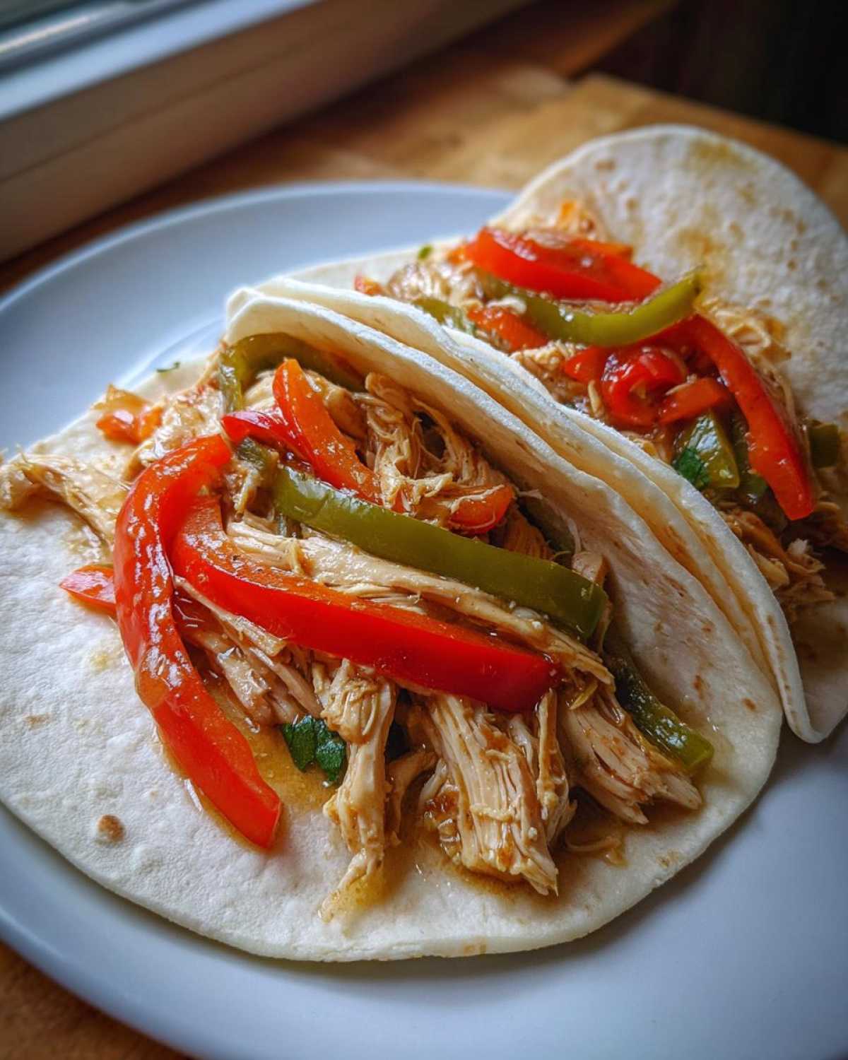 Two soft flour tortillas filled with shredded chicken, red, and green peppers for crockpot chicken fajitas.