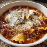 Close-up of a white bowl filled with rich crockpot lasagna soup, topped with melted mozzarella and herbs.