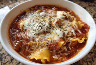 Close-up of a white bowl filled with rich crockpot lasagna soup, topped with melted mozzarella and herbs.