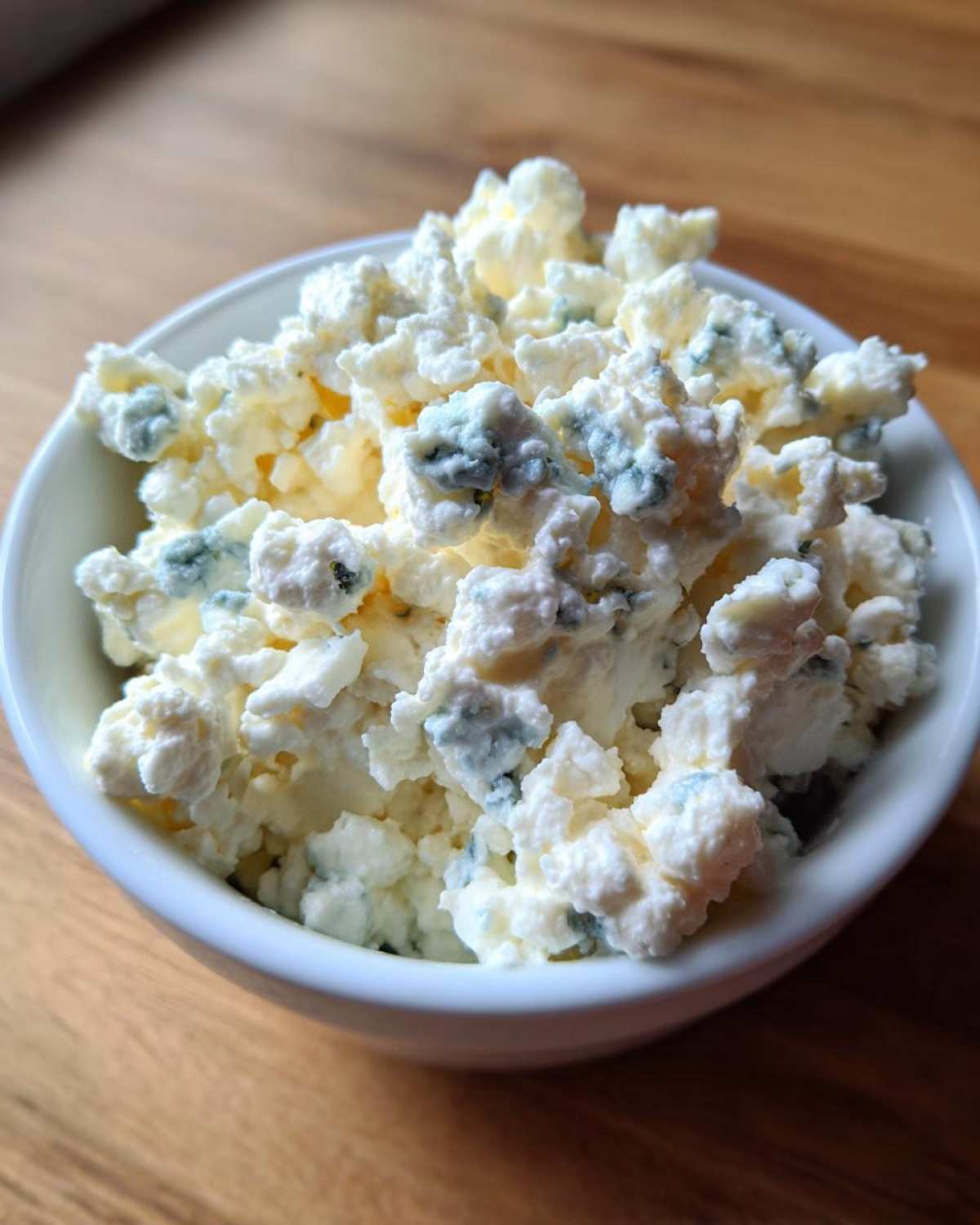 Close-up of crumbled blue cheese with visible blue veins in a small white bowl.