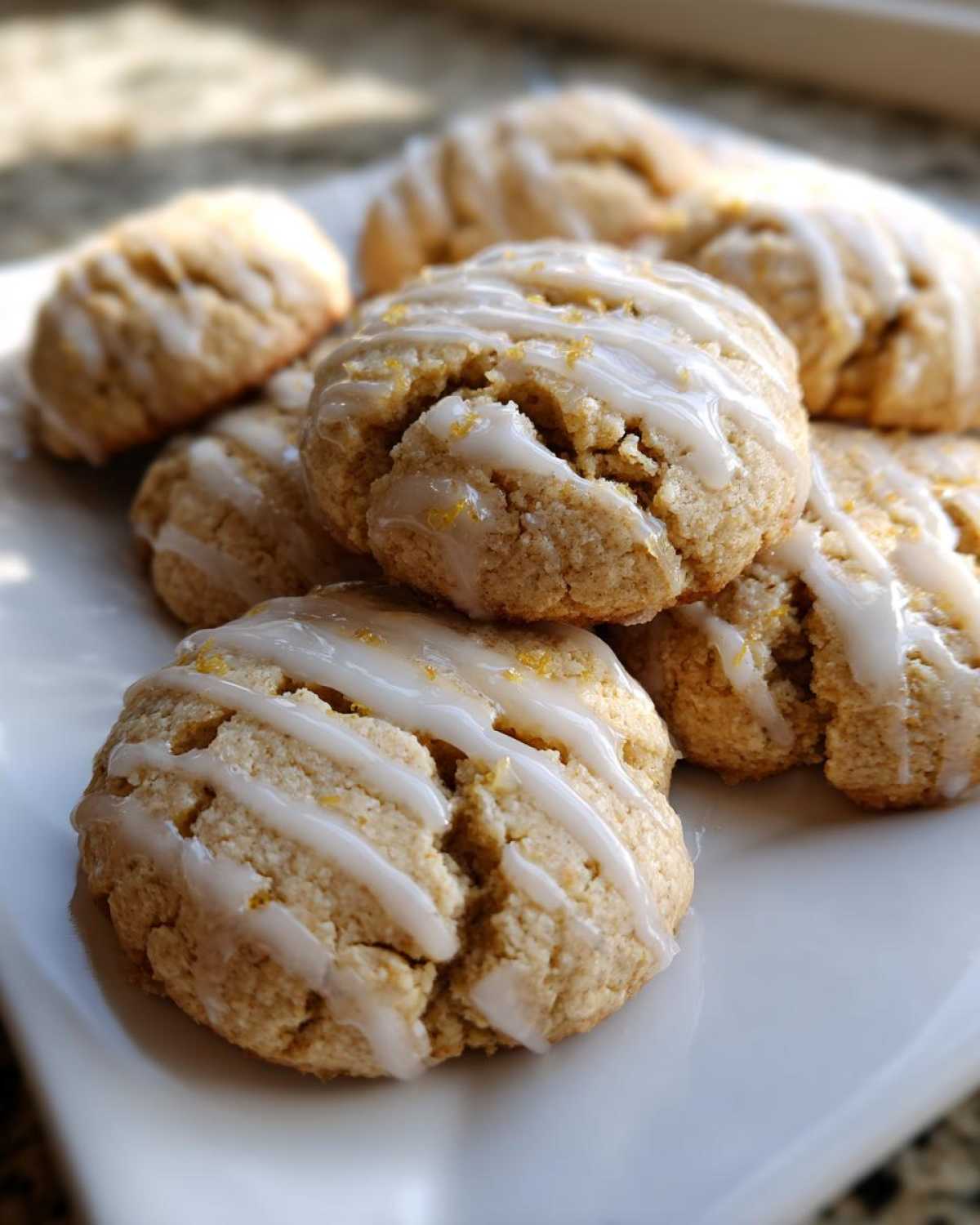 Close-up of several soft Earl Grey cookies drizzled with white lemon glaze and sprinkled with zest.