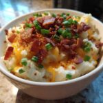 A bowl of creamy potato soup topped with melted cheddar cheese, bacon bits, and green onions, representing easy crockpot potato soup.