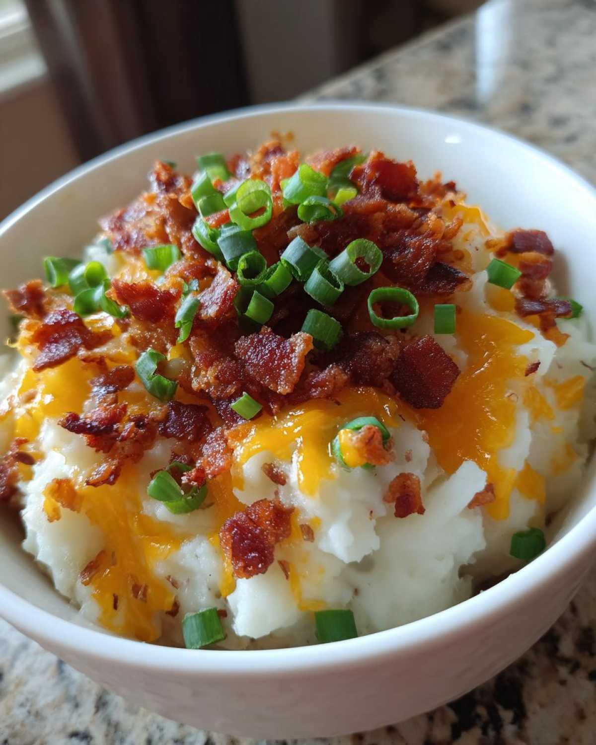 Close-up of creamy easy crockpot potato soup topped with melted cheddar, bacon bits, and green onions.