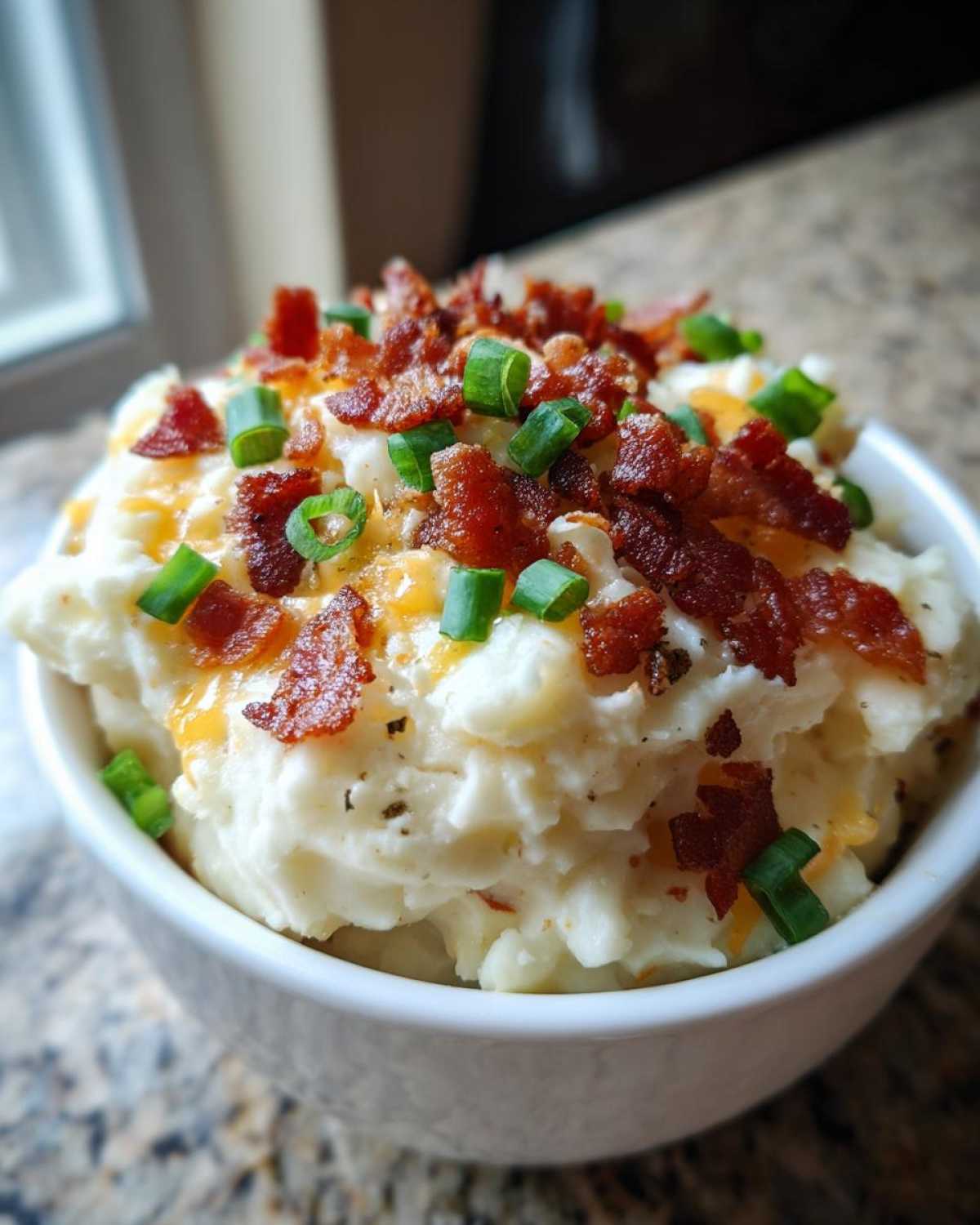 A bowl of thick, creamy easy crockpot potato soup topped with bacon, cheese, and green onions.