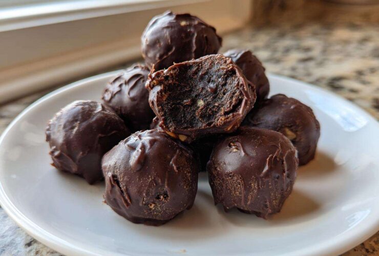 A pile of rich, chocolate-covered pecan pie balls on a white plate, one is broken open showing the filling.