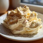 A generous swirl of light yellow, fluffy honey butter, dusted lightly with cinnamon, served on a white plate.
