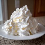 A large, beautifully piped mound of white vanilla buttercream frosting sitting on a white plate.