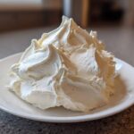 A generous mound of freshly piped, fluffy vanilla buttercream frosting sitting on a small white plate.