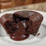 A rich chocolate lava cake cut open to reveal the gooey, molten center flowing onto a white plate.