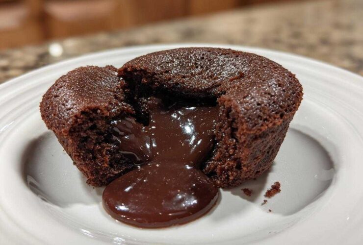 A rich chocolate lava cake cut open to reveal the gooey, molten center flowing onto a white plate.
