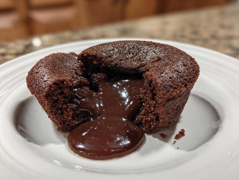 A rich chocolate lava cake cut open to reveal the gooey, molten center flowing onto a white plate.