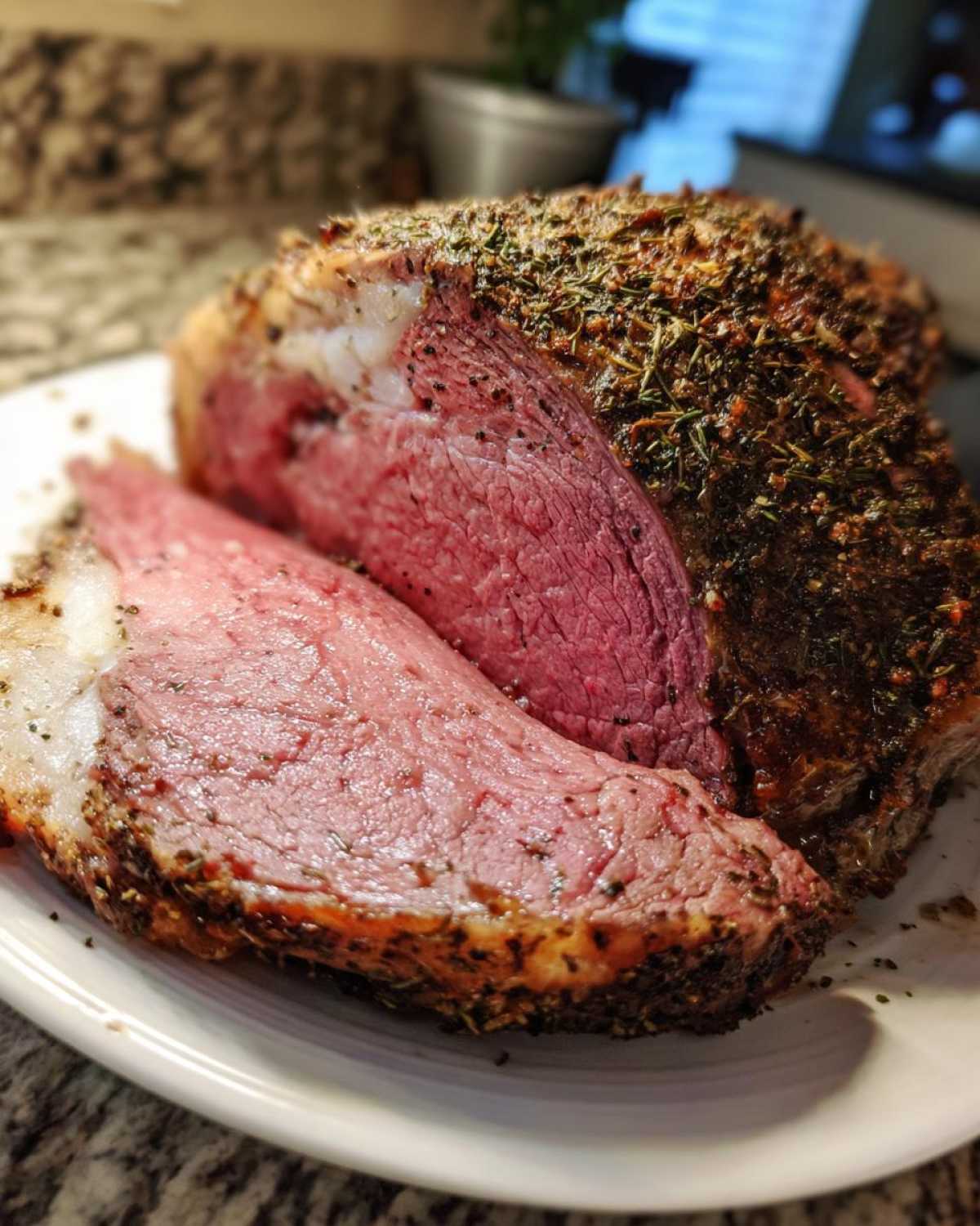 Close-up of a thick slice of medium-rare prime rib recipe roast with a dark herb crust.
