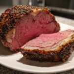 A juicy, medium-rare prime rib recipe roast, sliced to show the pink center and dark herb crust.
