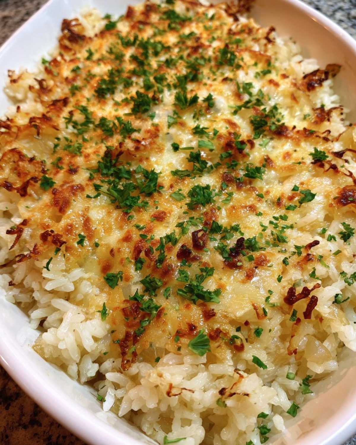 Close-up of baked french onion butter rice topped with melted, browned cheese and fresh parsley.