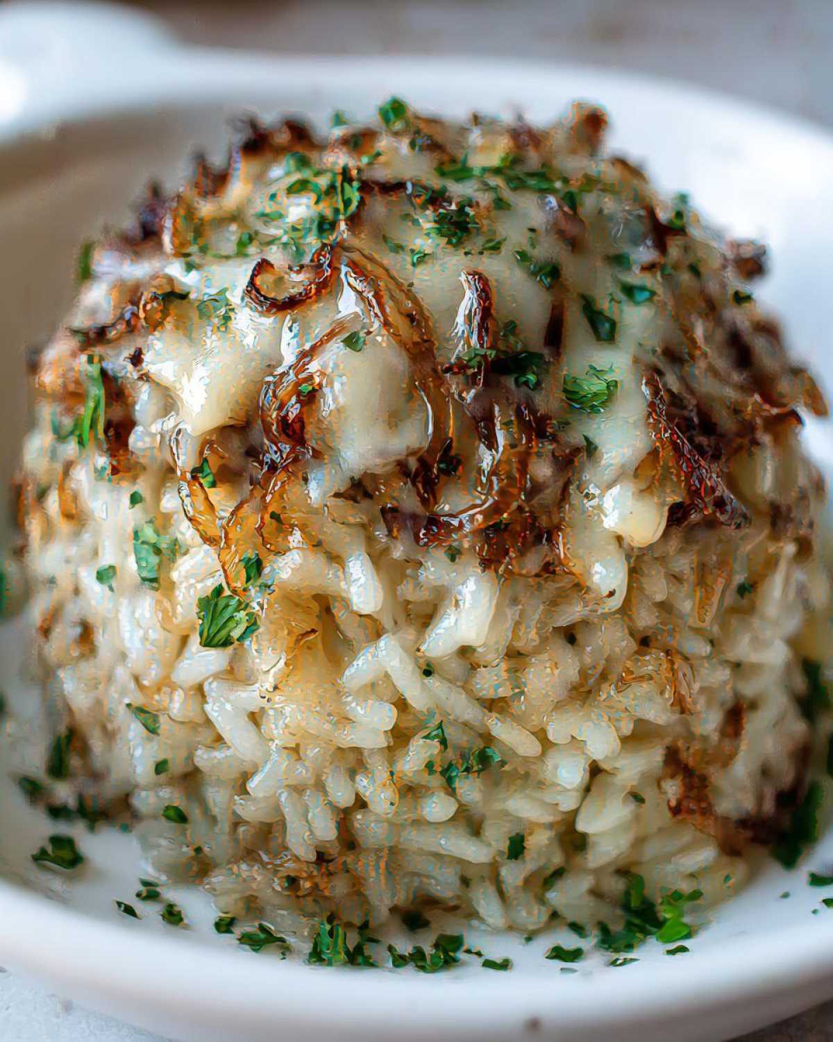 Close-up of french onion butter rice topped with melted cheese, caramelized onions, and fresh parsley.