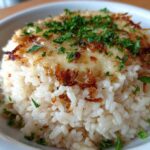 A close-up of a serving of fluffy french onion butter rice topped with melted cheese and crispy onions.