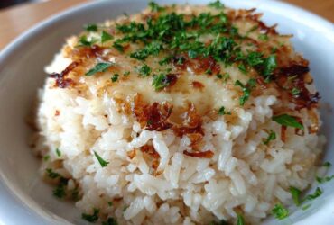 A close-up of a serving of fluffy french onion butter rice topped with melted cheese and crispy onions.