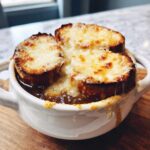 Close-up of a white crock filled with rich french onion soup topped with melted, browned cheese over toasted bread.