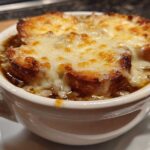 Close-up of a bowl of rich french onion soup topped with toasted bread and bubbly, melted Gruyère cheese.