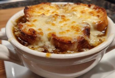 Close-up of a bowl of rich french onion soup topped with toasted bread and bubbly, melted Gruyère cheese.