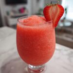 A vibrant, frozen strawberry daiquiri in a stemmed glass, garnished with a fresh strawberry slice.