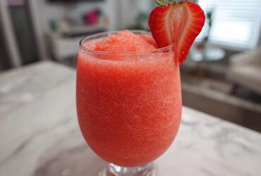 A vibrant, frozen strawberry daiquiri in a stemmed glass, garnished with a fresh strawberry slice.