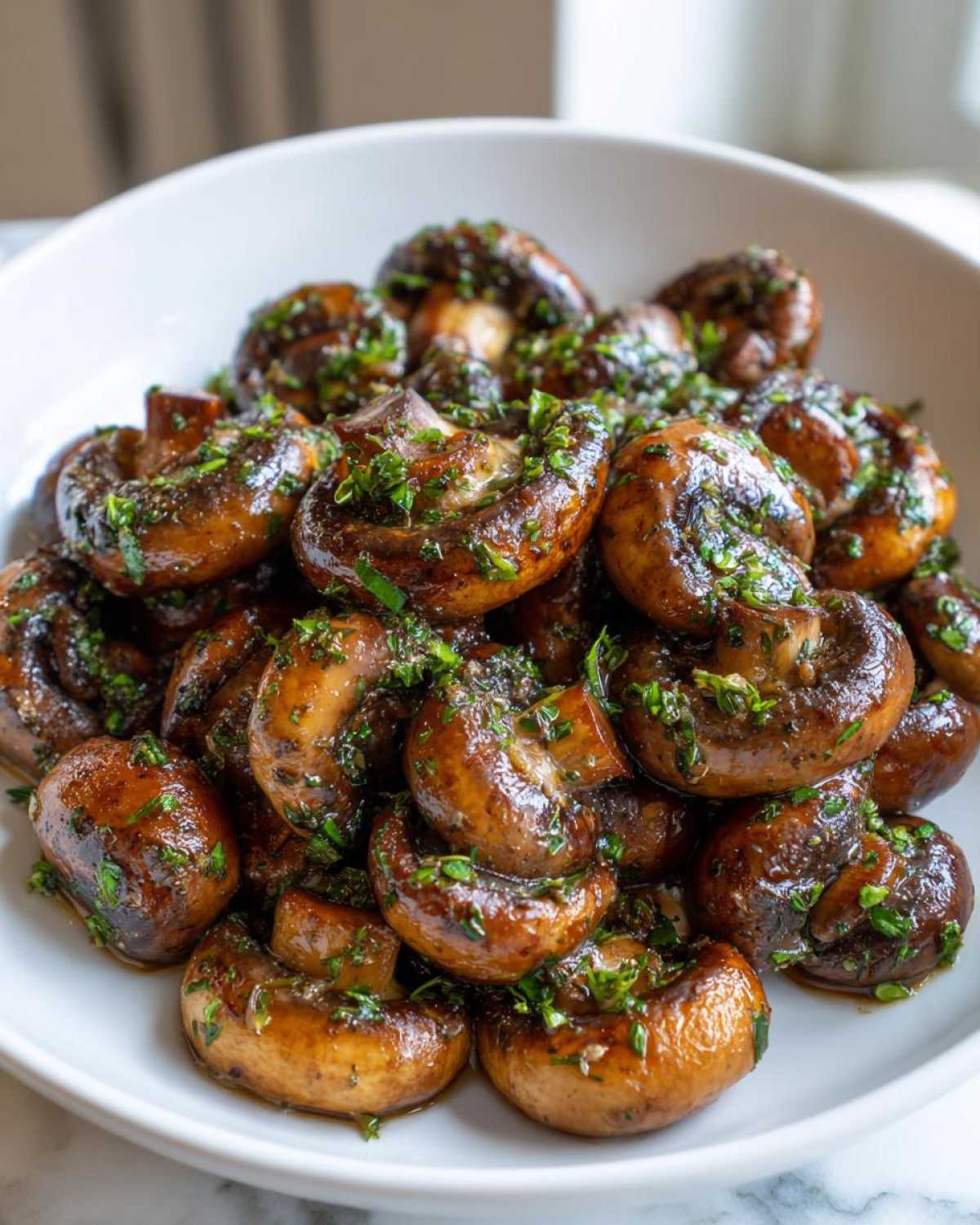 A close-up of a white bowl filled with glossy, sautéed garlic butter mushrooms topped generously with fresh chopped parsley.