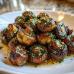 A close-up of a mound of savory garlic butter mushrooms, glistening with sauce and topped with fresh parsley.