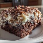 Close-up of a rich, moist slice of german chocolate poke cake with gooey topping on a white plate.