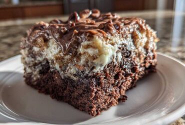 Close-up of a rich, moist slice of german chocolate poke cake with gooey topping on a white plate.