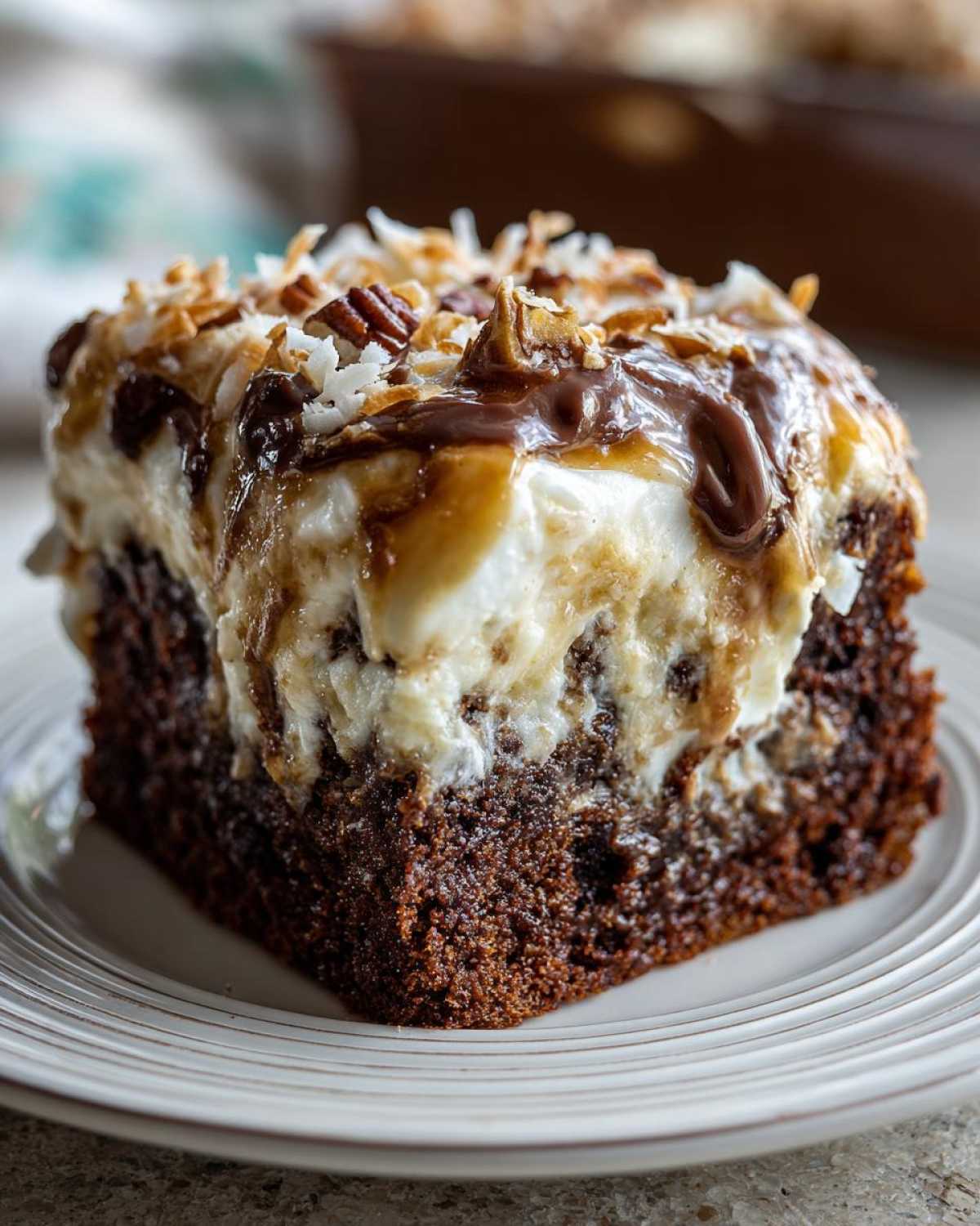 Close-up of a moist slice of german chocolate poke cake topped with creamy frosting, chocolate, and pecans.