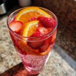 Close-up of a fizzy glass of champagne punch garnished with fresh strawberries and orange slices.