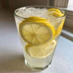 Close-up of a tall glass filled with bubbly, ice-cold lemonade and several bright yellow lemon slices.