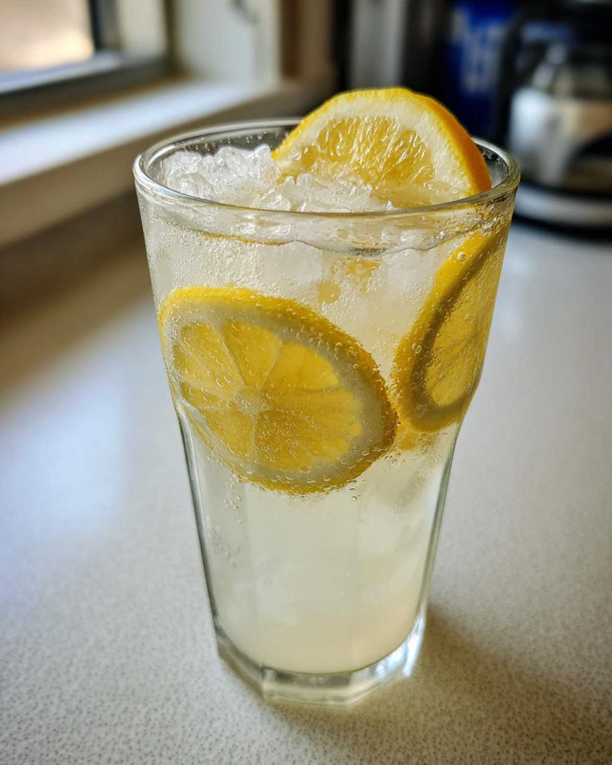 Close-up of a tall glass filled with sparkling lemonade, crushed ice, and fresh lemon slices.