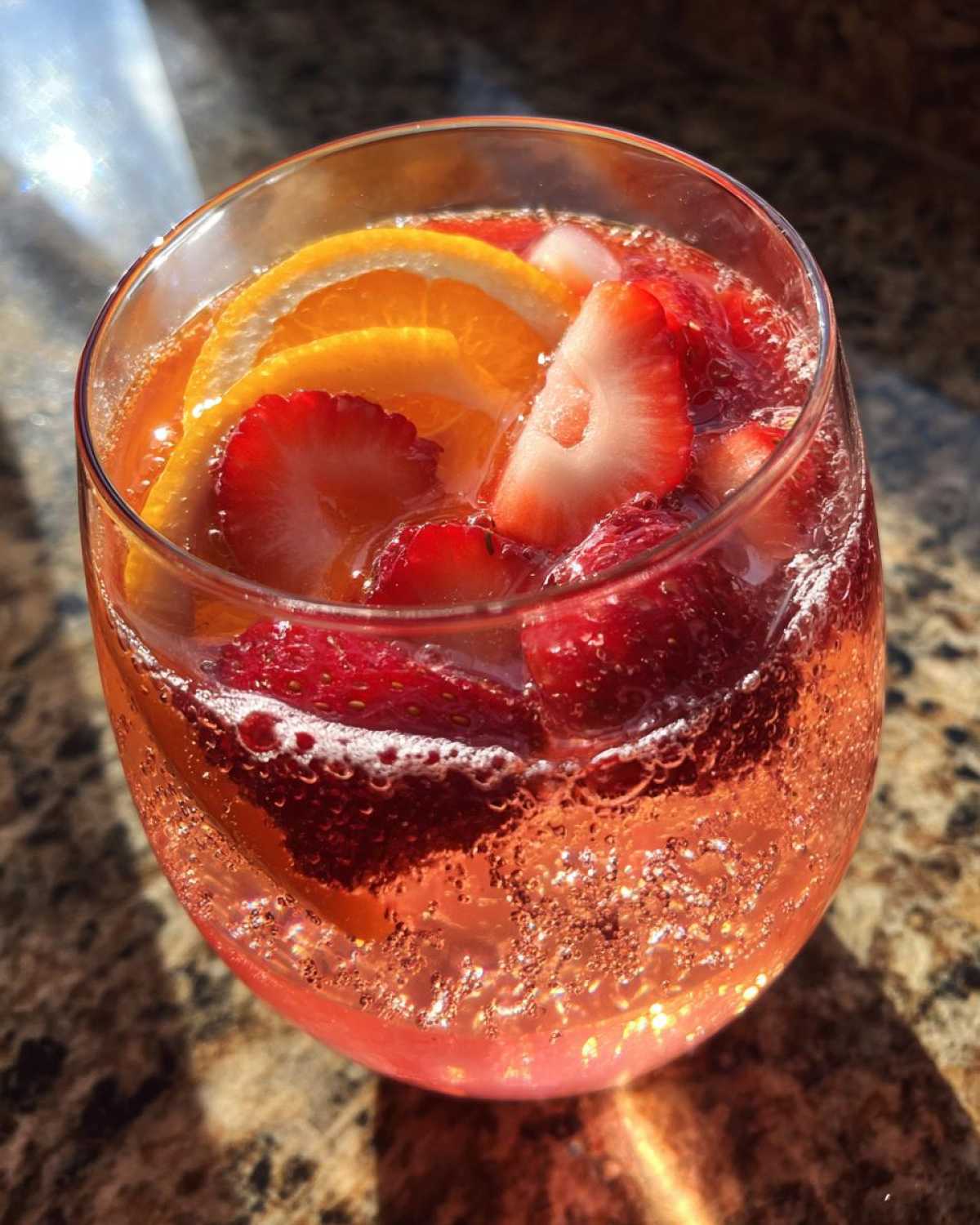 Close-up of a bubbly glass filled with pink champagne punch, garnished with fresh strawberry slices and orange rounds.